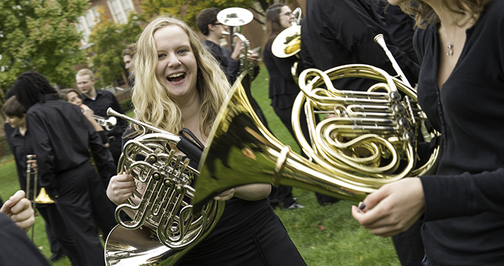 Blonde girl smiling holding trumpet in crowd outdoors with other band students