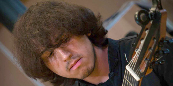Young man Sam Gracida with long brown hair playing guitar