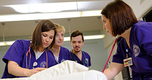 nursing students in capital uniforms standing around a patient bed