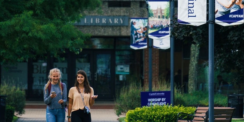 two college girls walking together down capital university path in front of library