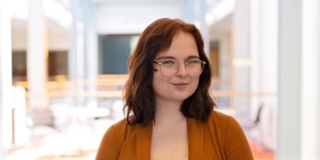 Photo of Liv Rafferty, a smiling brunette girl wearing glasses in an orange top